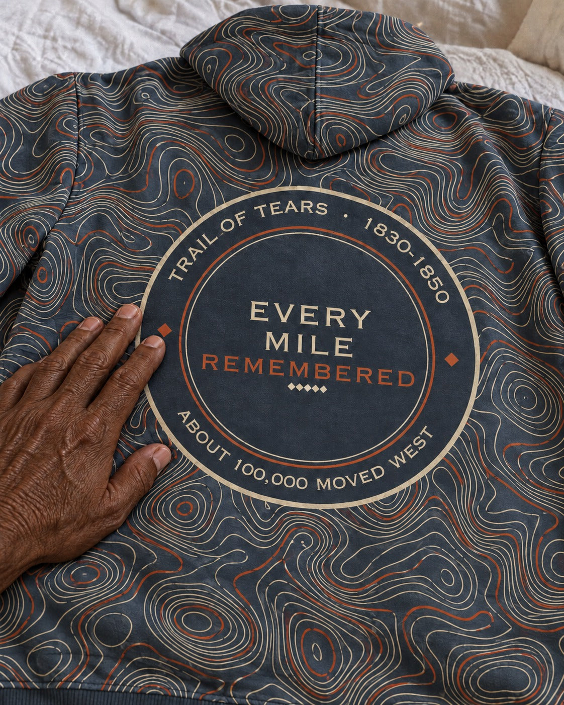 Hand resting on the back print of the Every Mile Remembered hoodie