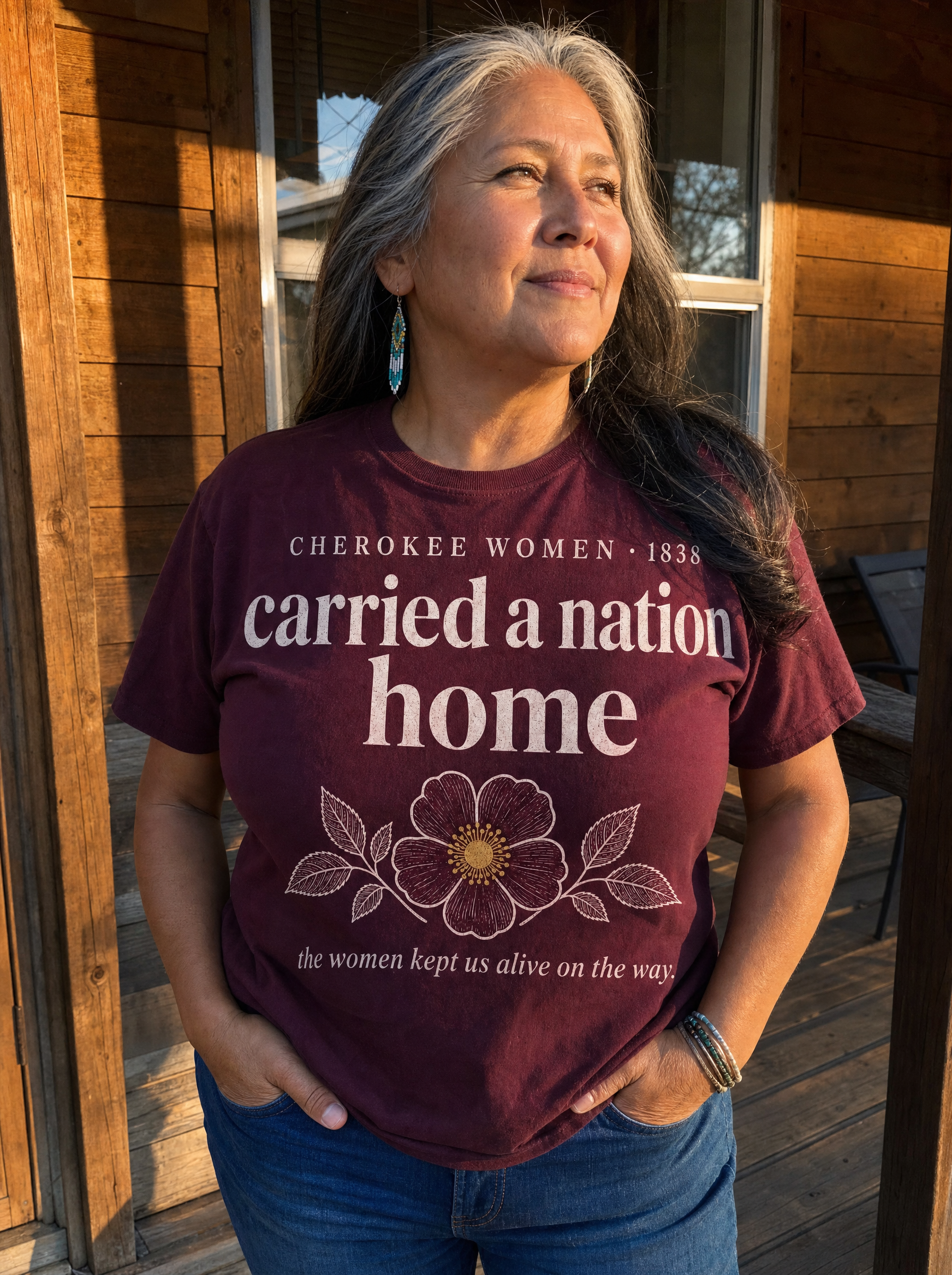 Elder woman wearing the Cherokee Women maroon heritage tee on a porch
