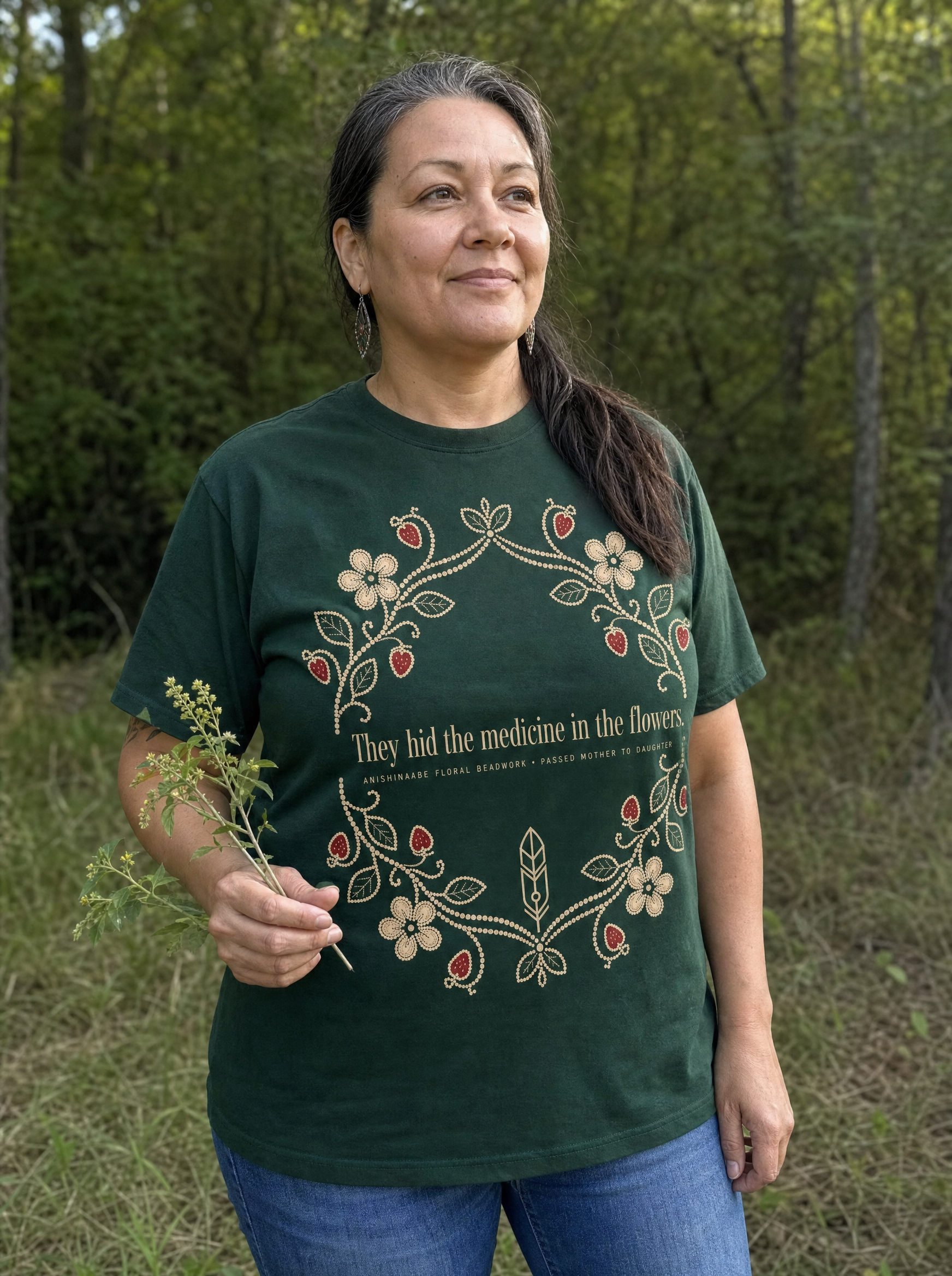 Woman wearing the Medicine in the Flowers forest-green Anishinaabe tee holding plants