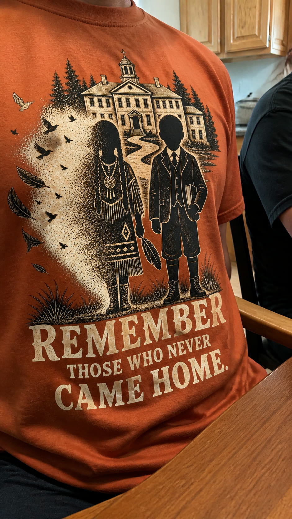 Two people talking at a kitchen table, one wearing the tee